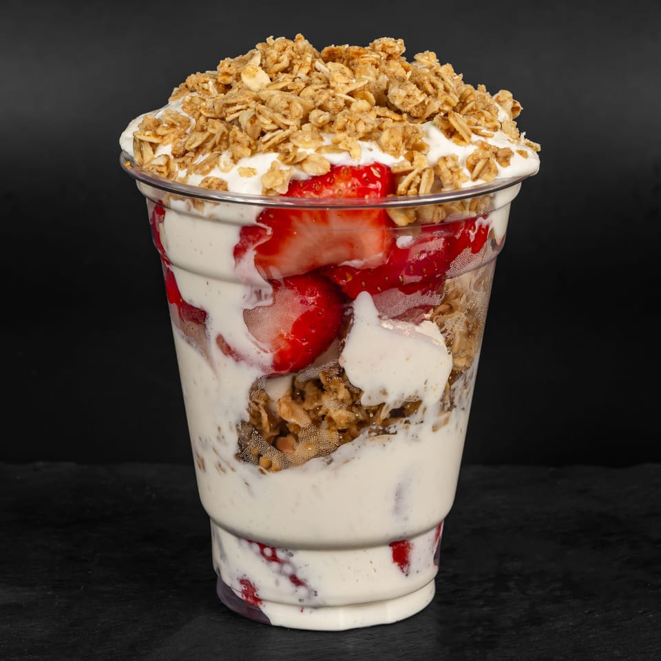 A Drizzle Cafe strawberry parfait with yogurt, granola, and fresh strawberries in a clear cup.
