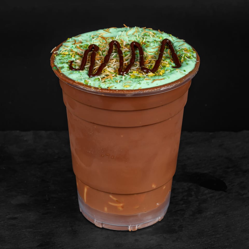 Drizzle Cafe's chocolate drink with green topping, chocolate drizzle, and sprinkles on a dark background.