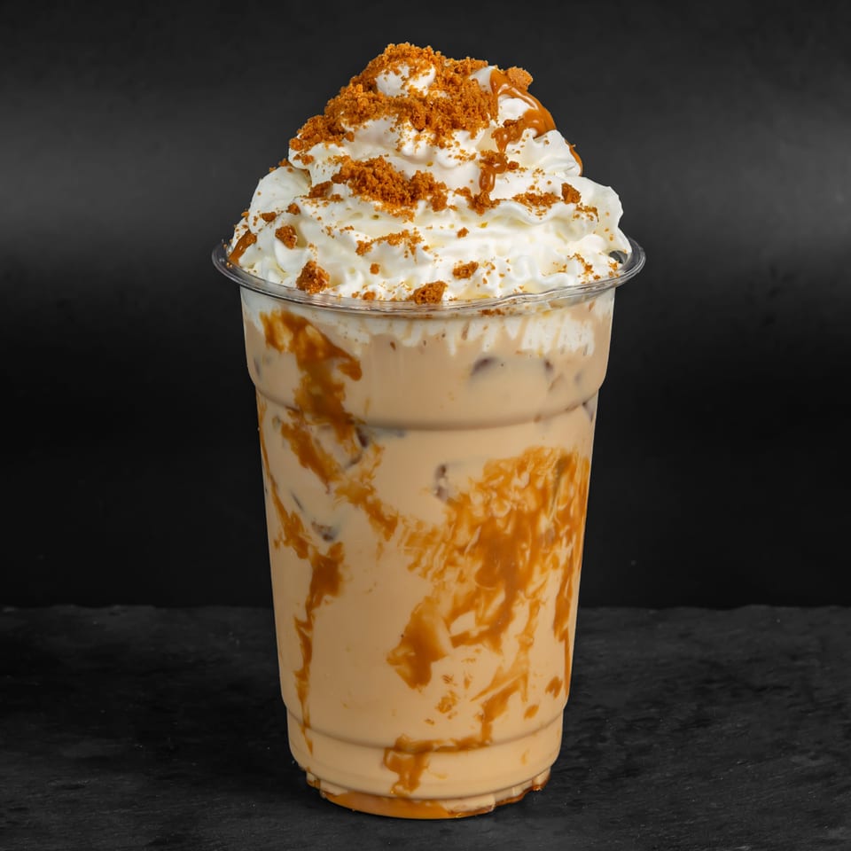 Iced coffee with whipped cream, caramel drizzle, and cookie crumbles in a clear plastic cup.