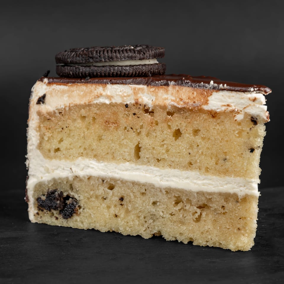 A slice of Drizzle Cafe's vanilla cake with white frosting, chocolate ganache, and an Oreo cookie.