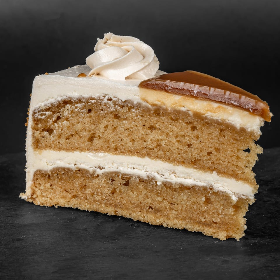 A slice of Drizzle Cafe's layered cake with white frosting, caramel, and a cream swirl.