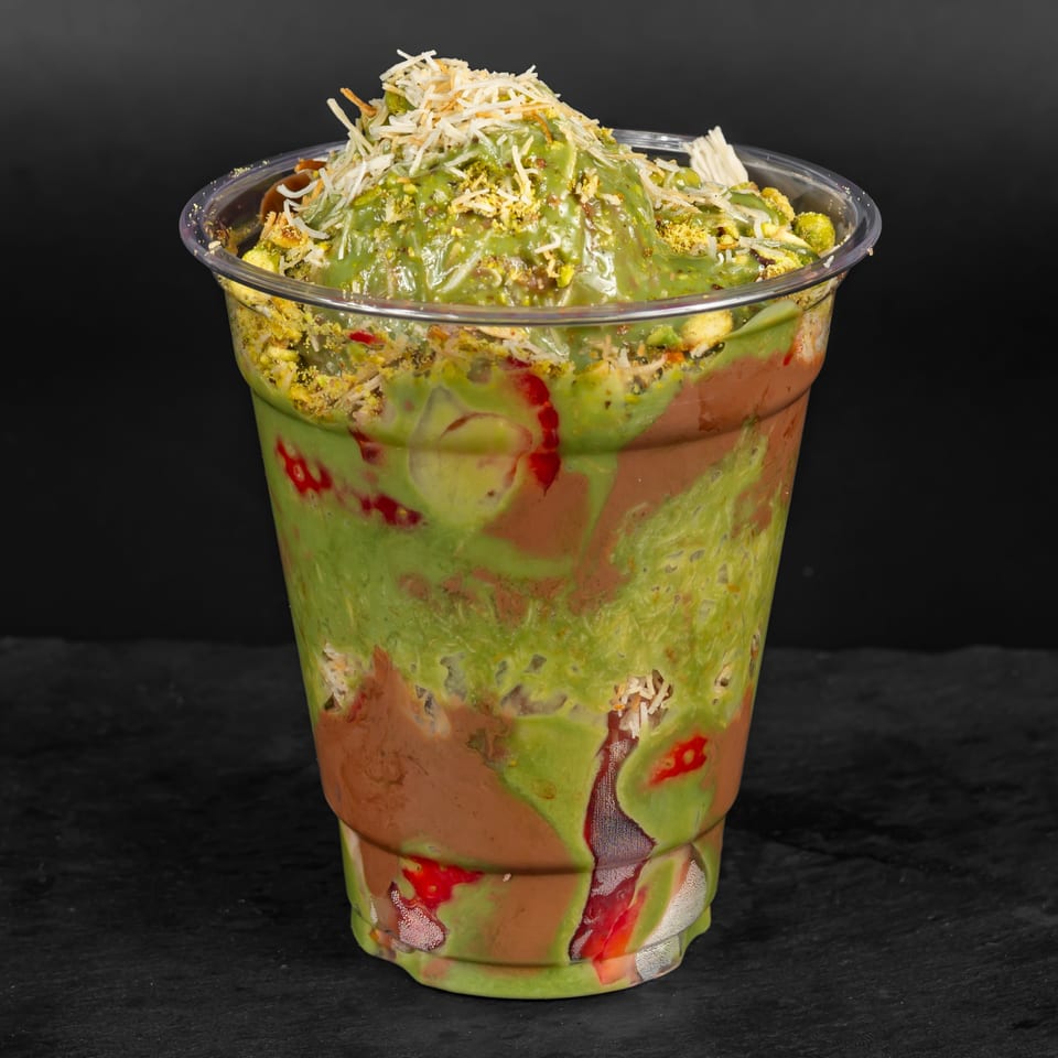 A Drizzle Cafe dessert cup with green and brown layers, topped with shredded coconut and pistachios.