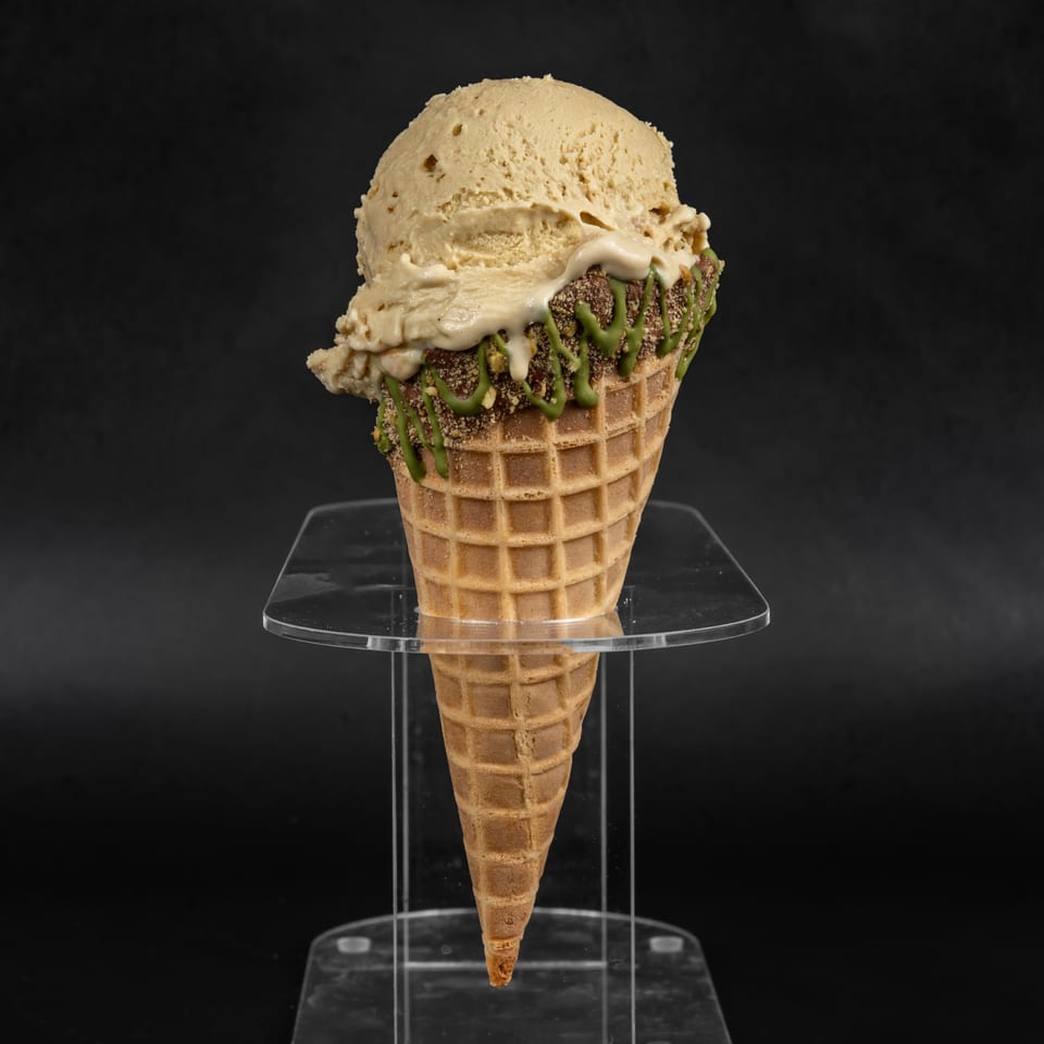 A waffle cone with two scoops of Drizzle Cafe's ice cream, drizzled with green and white sauce.